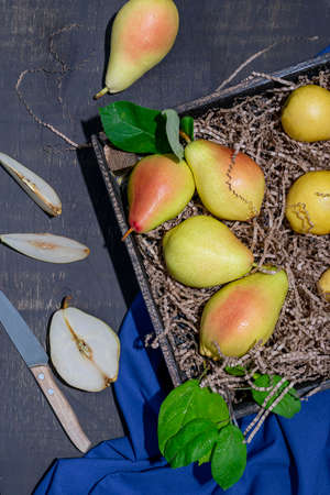 Yellow-red ripe pears lie in a wooden box with craft paper. Pear halves and a knife in the backgroundの写真素材