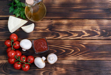 Red, juicy cherry tomatoes, champignons, hard cheese, olive oil and parsley greens lie on dark wooden boardsの写真素材