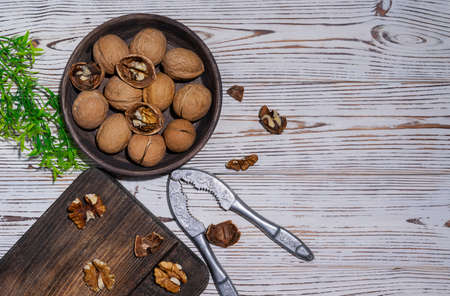 Ripe walnuts in a dark brown wooden bowl on a light wooden table