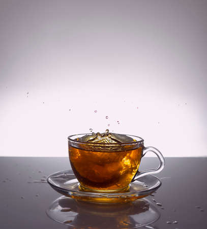 Splashes of tea are flying from a transparent glass cupの写真素材