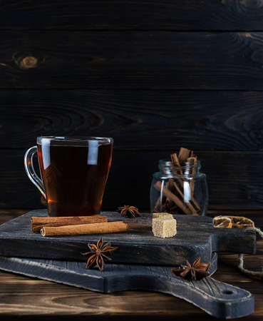 Hot aromatic tea with cinnamon and star anise in a transparent cup on dark wooden boardsの写真素材