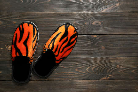 A pair of soft slippers with a tiger print on a dark brown wooden background. Top view, space for textの写真素材