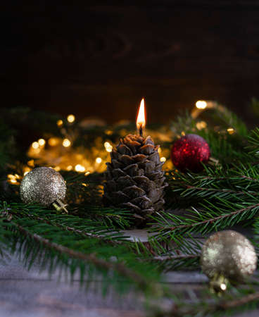 A candle in the form of a brown cone burns against the background of fir branchesの写真素材