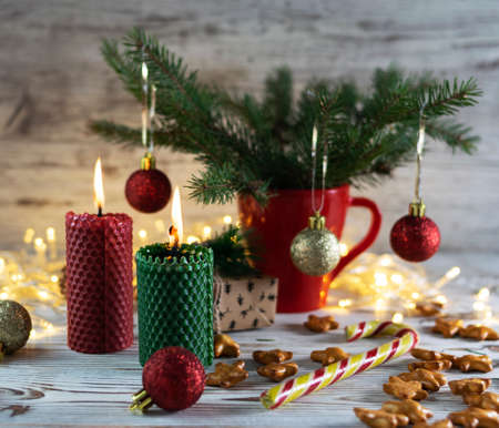 Red and green candle made of natural wax with Christmas balls on a light wooden tableの写真素材