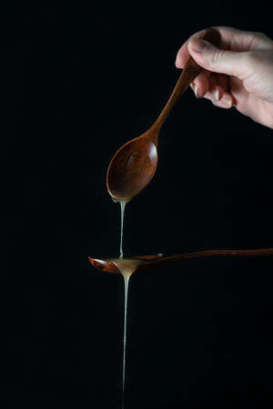 Honey is poured onto a wooden spoon. Black background. Transparent honey drips from a spoon. The hand holds a wooden spoon dripping with honeyの写真素材