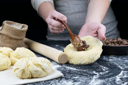 Hands put the filling on a rolled piece of dough with a wooden spoon. Flour with a canvas bag,...