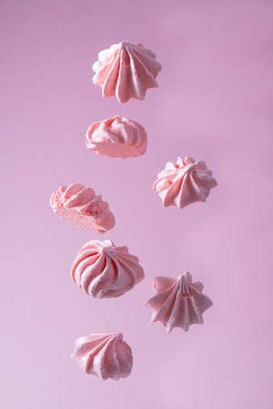 Pink meringue cookies are hanging in the air. Levitan food. Flying meringue. Pink background
