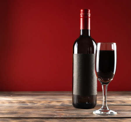 Red wine with a transparent high glass on a light wooden table. A bottle of wine in the background. red background. Place for textの写真素材