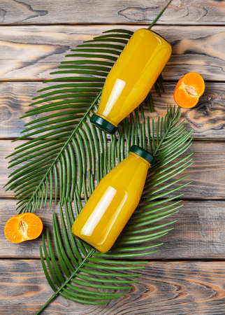 Two transparent bottles of tangerine juice lie on palm leaves. Tangerine halves on a light brown wooden table. top viewの写真素材
