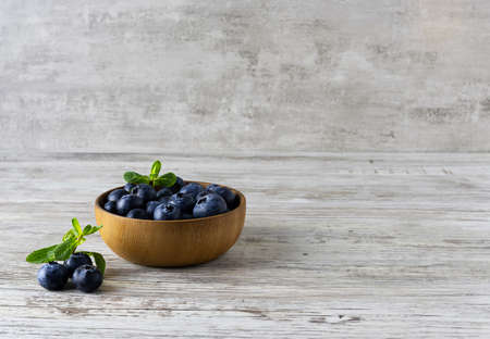 Blueberries in a wooden bowl with a sprig of mint on a light wooden table. Fresh large berries on the table. Light wooden background. Space for textの写真素材