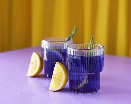 Tea with ice from clitoria flowers in transparent glasses on a lilac table. Slices of lemon next to the glasses. Sprigs of rosemary in the background. yellow backgroundの写真素材
