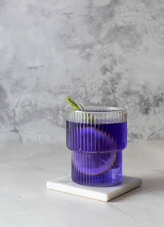 Tea from clitoria flowers with ice, lemon and rosemary on a light table. Glass glass on a marble stand. light marble backgroundの写真素材