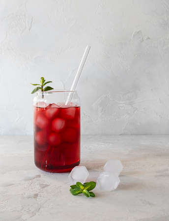 Red iced tea with a transparent glass with a straw on a light table. Ice cubes and mint leaves on the table. light backgroundの写真素材