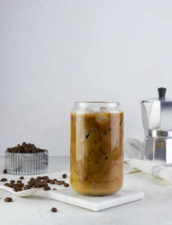 Cold coffee with milk in a transparent glass on a marble stand