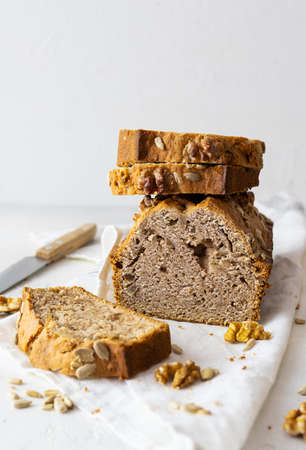 Fresh homemade bread with seeds and nuts on a light napkin. Walnuts on the table. A knife in the...