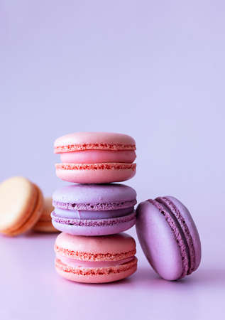 Pink and lilac macaroons are stacked on a lilac table. Beige macaroons in the background. purple...