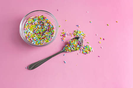 Multi-colored conduit sprinkle in a glass vase on a pink table. A teaspoon on the table. Light pink background. top viewの写真素材