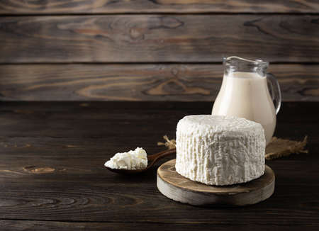 Fresh milk curd lies on a round wooden plank. A jug of milk in the background. Wooden spoon with...