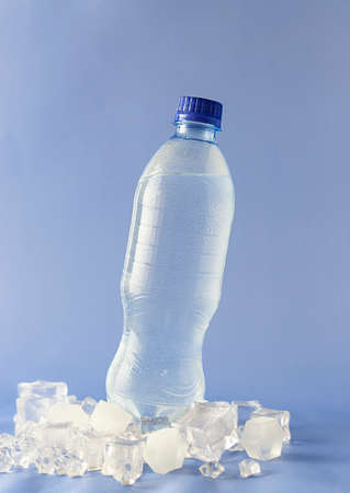 Transparent bottle with mineral water in ice cubes. Droplets of water on the bottle. light blue backgroundの写真素材