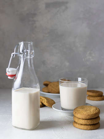 Oatmeal cookies and a glass of fresh milk on a light table. A bottle of milk in the foreground. Light gray background, text spaceの写真素材