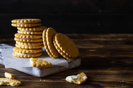 Crumbly cookies with cream filling lie in a stack on a wooden board