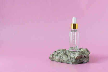 Bottle with liquid for the care of the skin of the face on the stone. Light pink background, text spaceの写真素材