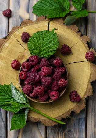 Large pink raspberries in a wooden bowl on a wooden stand. green leaves in the background. Light...