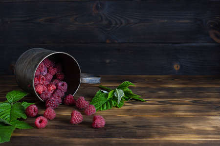 Large ripe raspberries in iron on a wooden table. green leaves in the background. Dark wooden background, space for textの写真素材