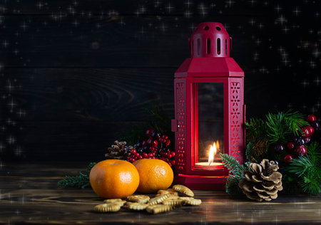 Red candlestick with a warming candle on a dark wooden table. Tangerines, cookies and red berries in the background. Dark wooden background with bokeh. Space for textの写真素材