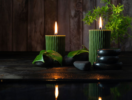 Two green candles with a bamboo pattern on a dark wooden table. Basalt stones with droplets in the background. Dark wooden background, space for textの写真素材