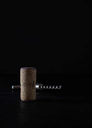 Natural wine cork of light brown color on a black table. A silver cork screw in the background....