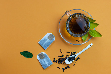 Tea bags made of clear paper lie on an orange table. Tea in a clear cup in the background. Dried tea leaves on the table. Top view, space for textの写真素材
