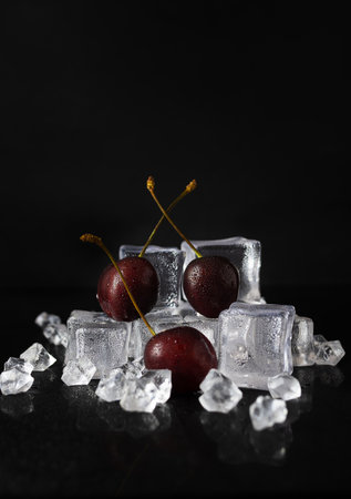Berries of ripe juicy cherries lie on transparent ice cubes. Crushed ice on a black table. dark background. Space for textの写真素材