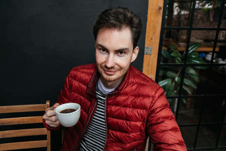 Handsome young man sitting on chair and drinking coffee in the restaurant. Portrait smiling and happy guyの写真素材