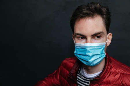 Portrait of an attractive caucasian man with surgical medical face mask who is concerned about preventing pandemic coronavirus on a black background.  Coronavirus Covid-19 concept. Protect your healthの写真素材