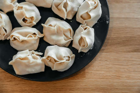 Stuffed homemade dumplings, manti of dough and minced on a dark plate on wooden table. Close up. Top view.の写真素材