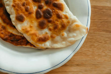 Homemade gold cheburek with meat on a white plate on wooden table