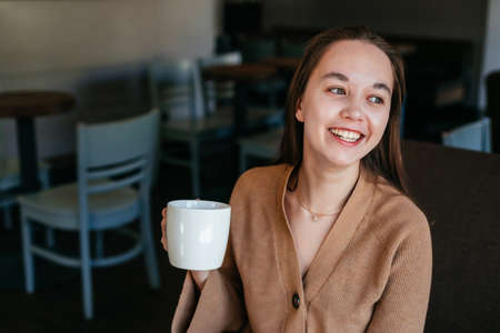 Close portrait of an attractive beautiful girl holding and drinking a cup of coffee in her hand and...
