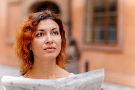 Pretty young female tourist with a map discovering history foreign city, looking to monuments. Woman holding city map. Solo girl travel in Europe.の写真素材