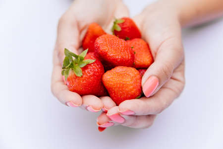 Close up of fresh red strawberries with green leave in woman hand on white scene. Selective focus