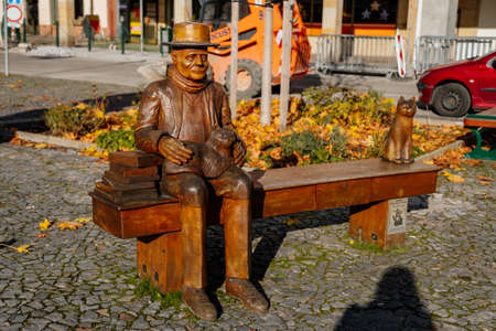 Wooden sculpture of Czech writer Bohumil Hrabal, Bohumil Hrabal sitting in the bench with a cat, Premyslid Square in sunny autumn day, Nymburk, Central Bohemia, Czech Republic, November 17, 2020のeditorial素材