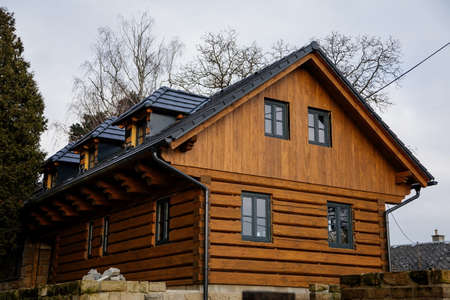 New home in village, Small old yellow and brown wooden house in Bohemian Paradise, dark tiled roof, traditional hut or cottage surrounded by trees in autumn forest, Czech Republic, December 05, 2020のeditorial素材