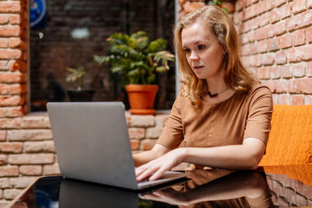 Attractive young elegant business woman spending time at cafe, working on laptop. Freelancer...