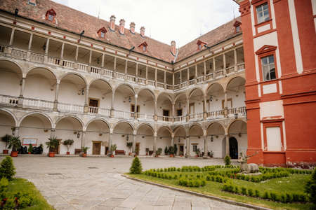 Opocno castle, renaissance chateau, courtyard with arcades and red facade, green lawn with statue and flowers in foreground, sunny summer day, aristocratic residence, Czech Republic, June 12, 2021のeditorial素材