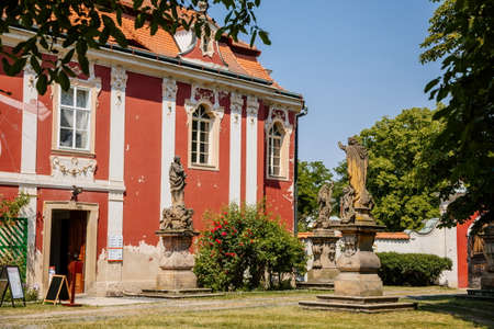 Baroque castle Steknik, stucco, peeling dark red plaster, red tile roof, green lawn, italian garden, aristocratic residence in summer sunny day, ancient chateau Steknik, Czech Republic, June 19, 2021のeditorial素材