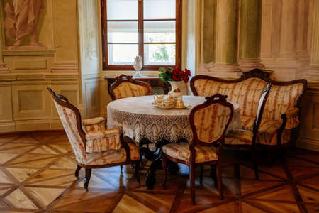 Rococo chateau interior, carved wooden furniture, armchairs and sofa, table set for tea, porcelain dishes, braided lace tablecloth, red roses in vase, Baroque castle Steknik, Czech Republic, June 19, 2021のeditorial素材