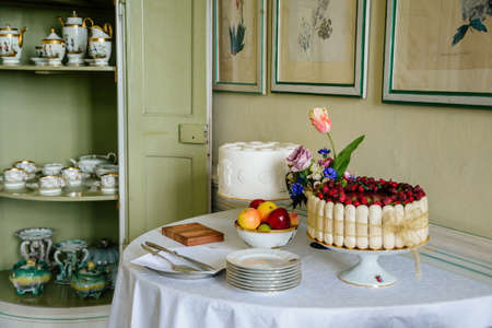 Krasny Dvur Chateau, North Bohemia, Czech Republic, 19 June 2021: Castle interior, white rococo furniture in dining room, baroque cupboard with dishes, cake and fruits on table.のeditorial素材