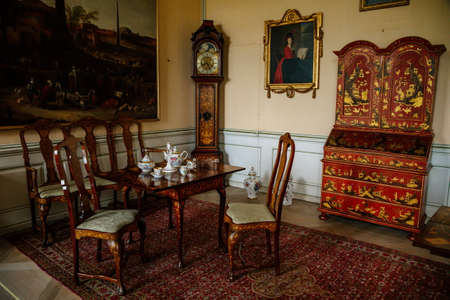 Krasny Dvur Chateau, North Bohemia, Czech Republic, 19 June 2021: Castle interior, baroque furniture, living room wooden carved table with chair and tea set, secretaire and antique grandfather clock.のeditorial素材