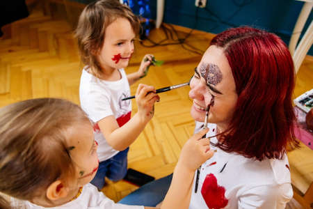 Family hobbies leisure activity home concept. Mother and small daughter drawing with fun using paintbrushes and watercolors. Children and parent creating picture together, body paint, home quarantine.の写真素材