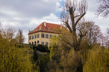 Prague, Czech Republic, 25 April 2021: gothic Chateau Mistodrzitelsky letohradek or Governors Summer Palace at the hill Stromovka park at spring day, blooming garden with pink sakura trees.のeditorial素材